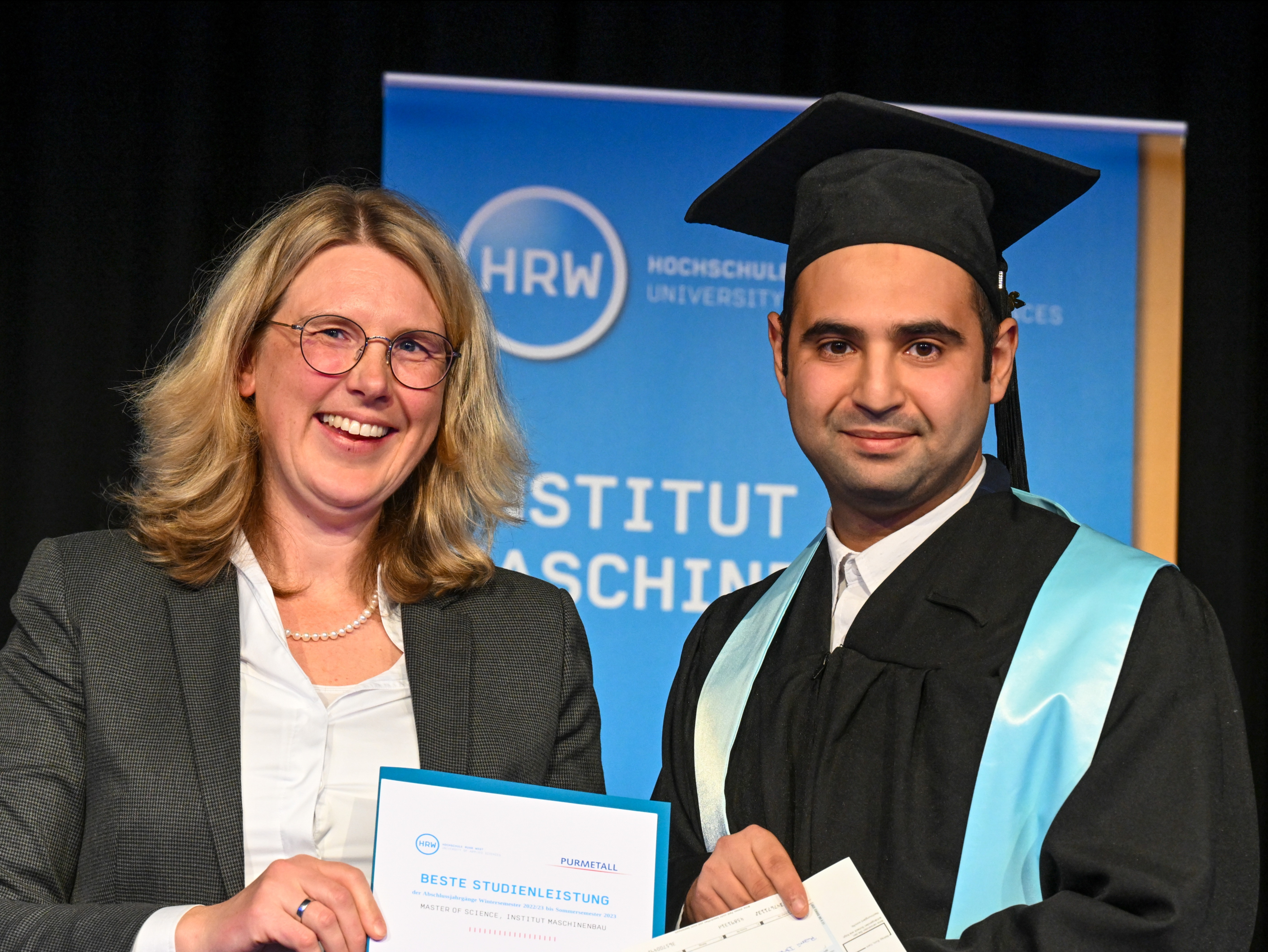 Foto: Ein Student erhält von einer Frau eine Auszeichnung mit der Aufschrift "Beste Studienleistung"