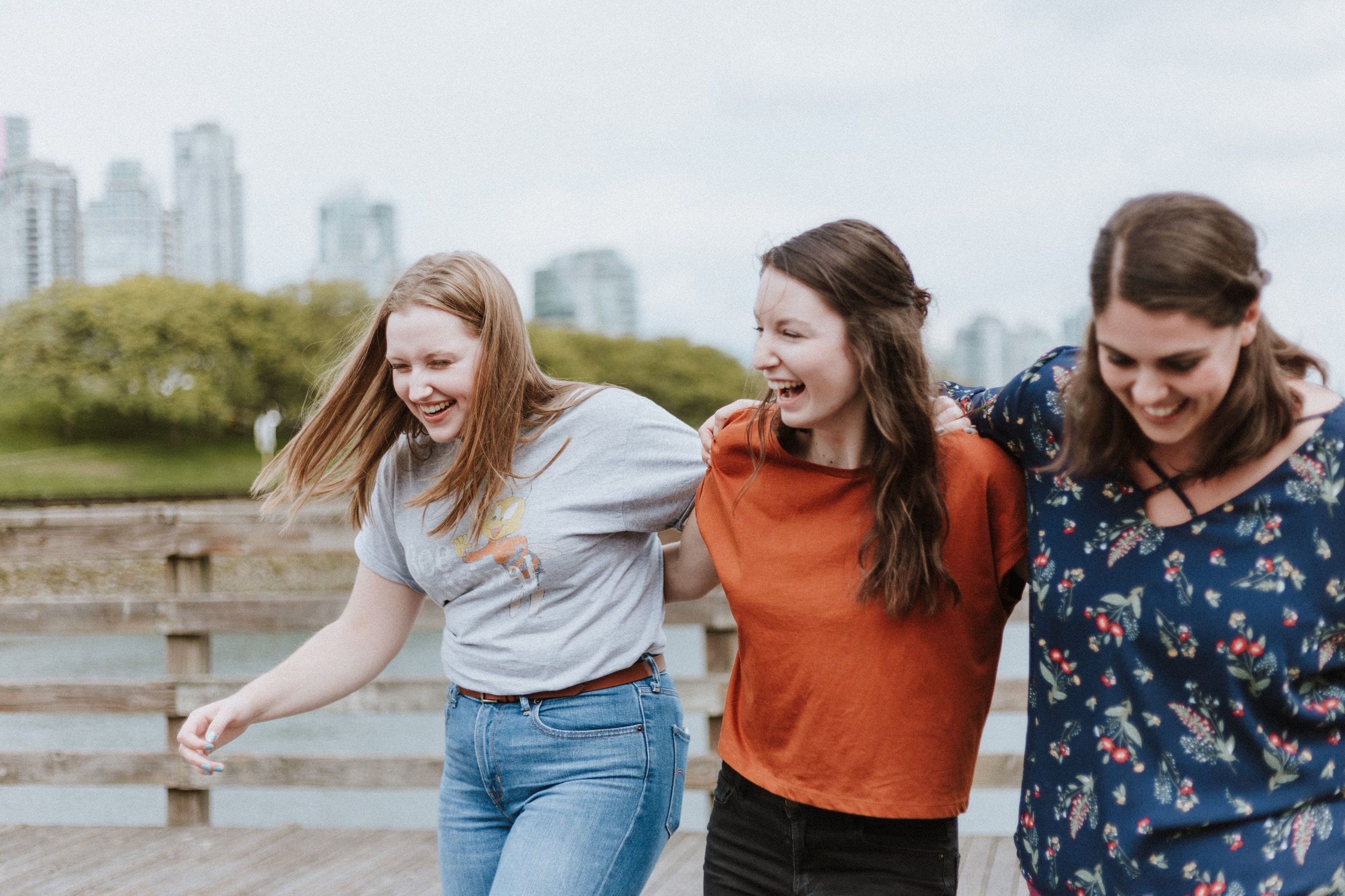 Drei glückliche Studentinnen die Arm in Arm miteinander lachen